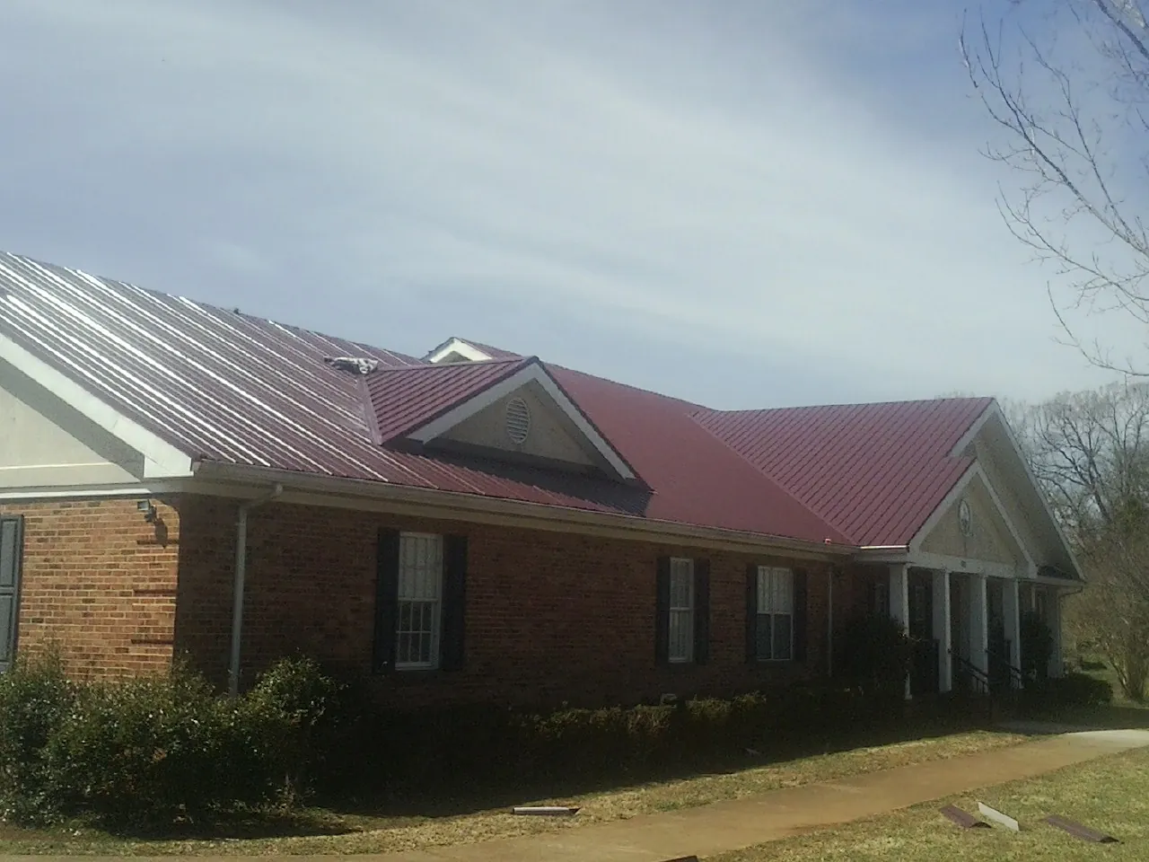 Red metal roof with gabled entries on a long brick building, from a Hail Damage Roof Repair job in Pillsbury