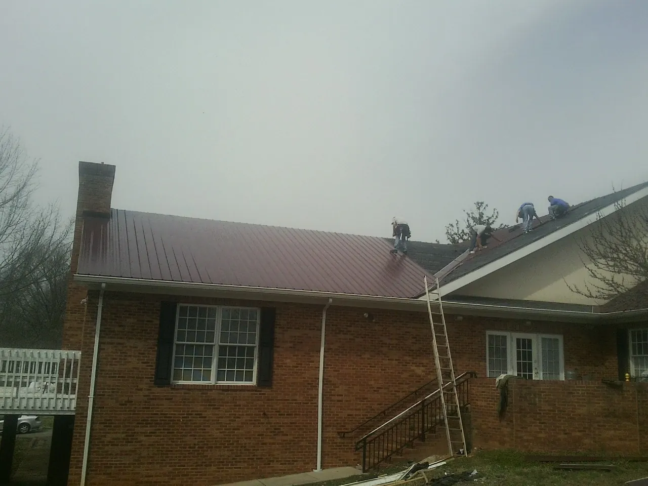 Crew setting red metal roofing panels on a brick home in Pillsbury