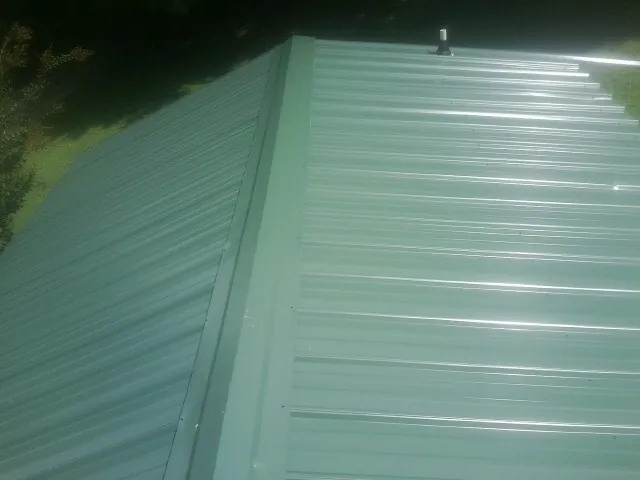New green metal panels meeting at the ridge of a roof — Flat Roof Repair work by our crew in Pillsbury