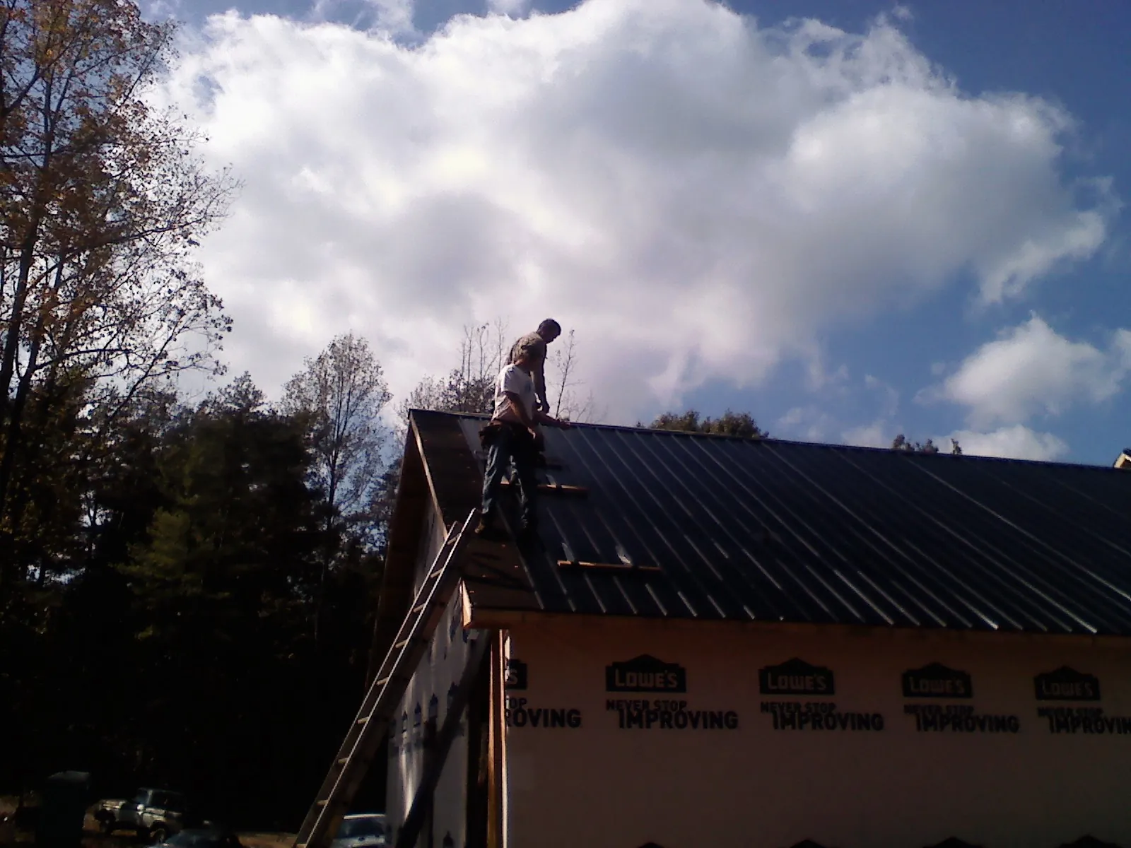 Roofer fastening dark metal panels high against a cloudy sky, from a Roof Inspection job in Pillsbury