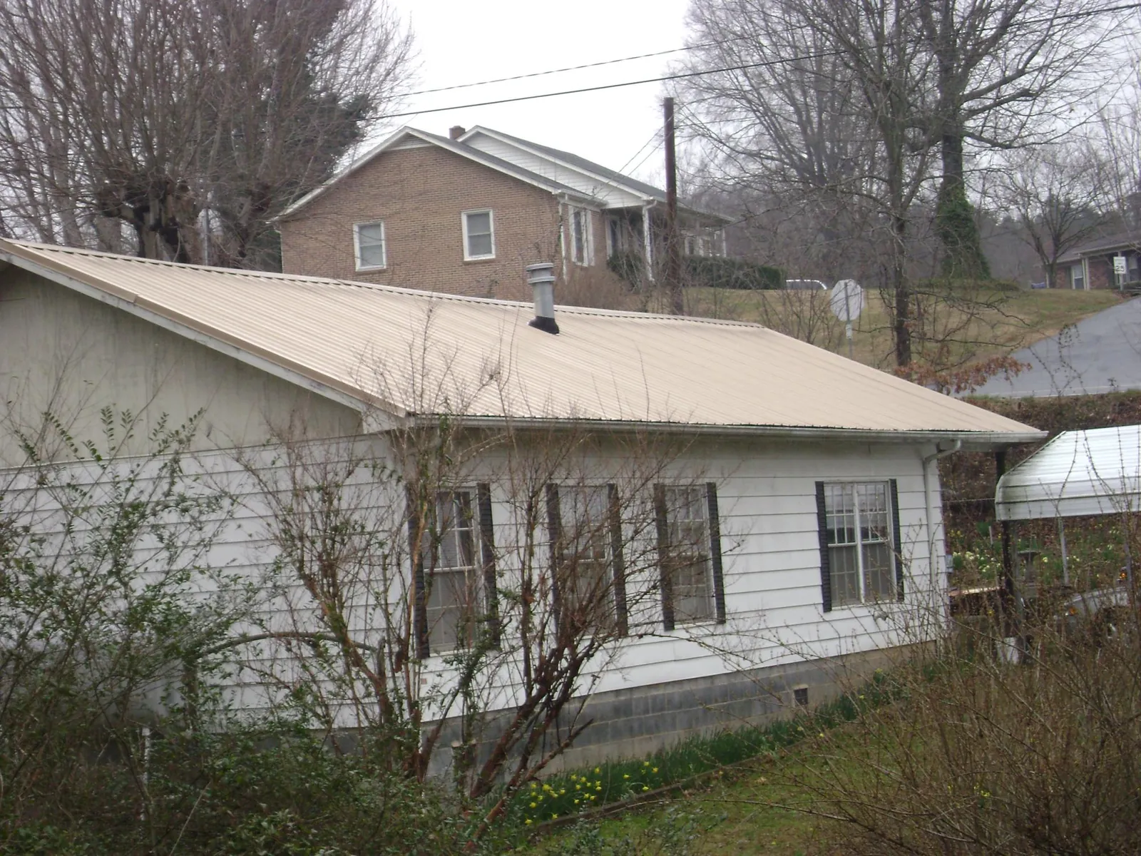 Tan metal roof on a white sided house set into a hillside — Commercial Roofing by Roofing Brothers in Pillsbury